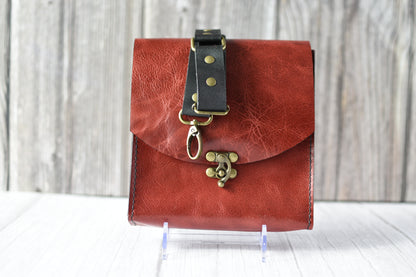 Red leather purse with a antique brass clasp on a white background with black leather strap