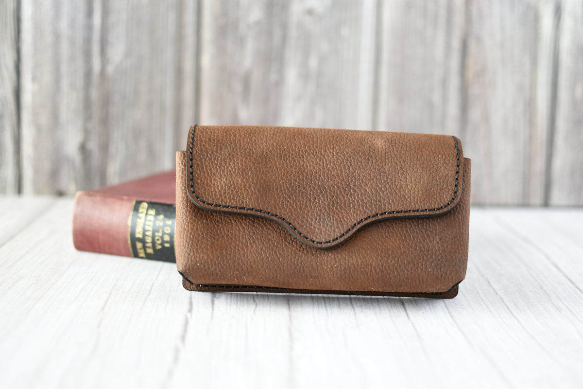 Brown leather cell phone purse on a wooden surface with a blurred background