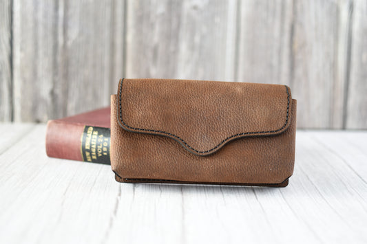 Brown leather cell phone purse on a wooden surface with a blurred background