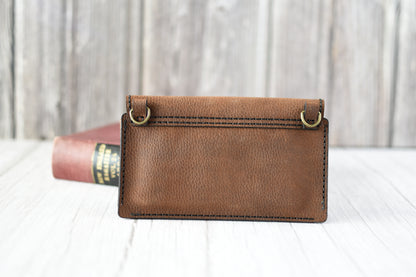 Brown leather cell phone purse on a wooden surface with a book in the background