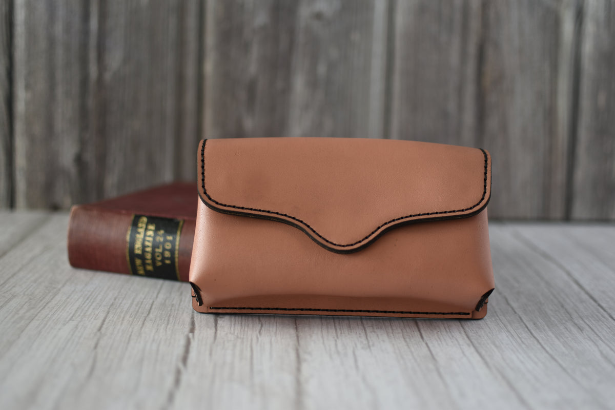 Brown leather cell phone purse on a wooden surface with a book in the background