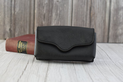 Black leather cell phone purse on a wooden surface with a book in the background