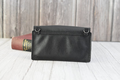 Black leather cell phone purse on a wooden surface with a book in the background