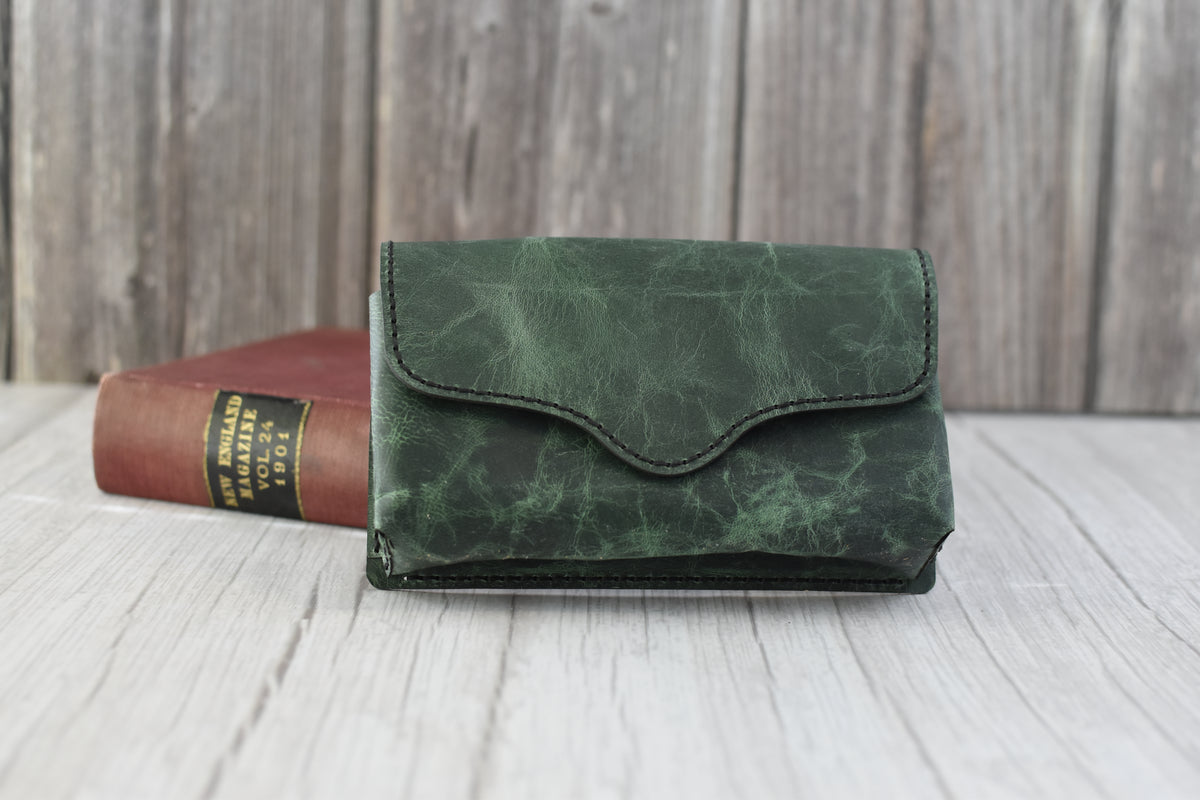 Green marbled leather cell phone purse on a wooden surface with a book in the background