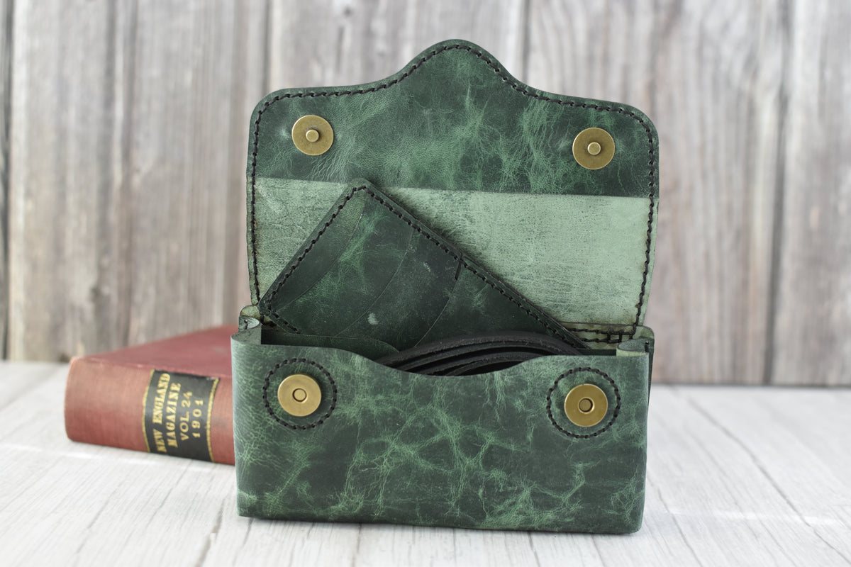 Green marbled leather cell phone purse on a wooden surface with a book in the background with compact wallet and black strap