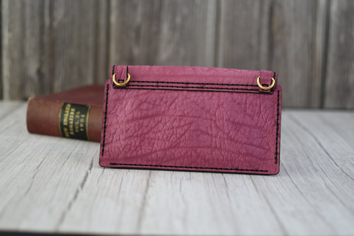 Pink leather cell phone purse on a wooden surface with a book in the background