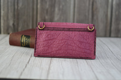 Pink leather cell phone purse on a wooden surface with a book in the background