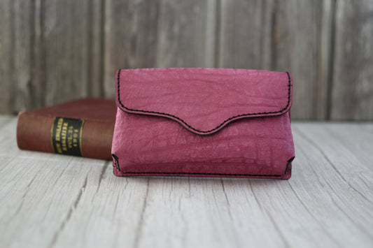 Pink leather cell phone purse on a wooden surface with a book in the background