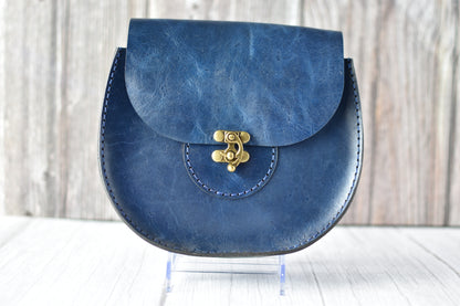 Blue leather saddle purse with a gold clasp on a wooden surface